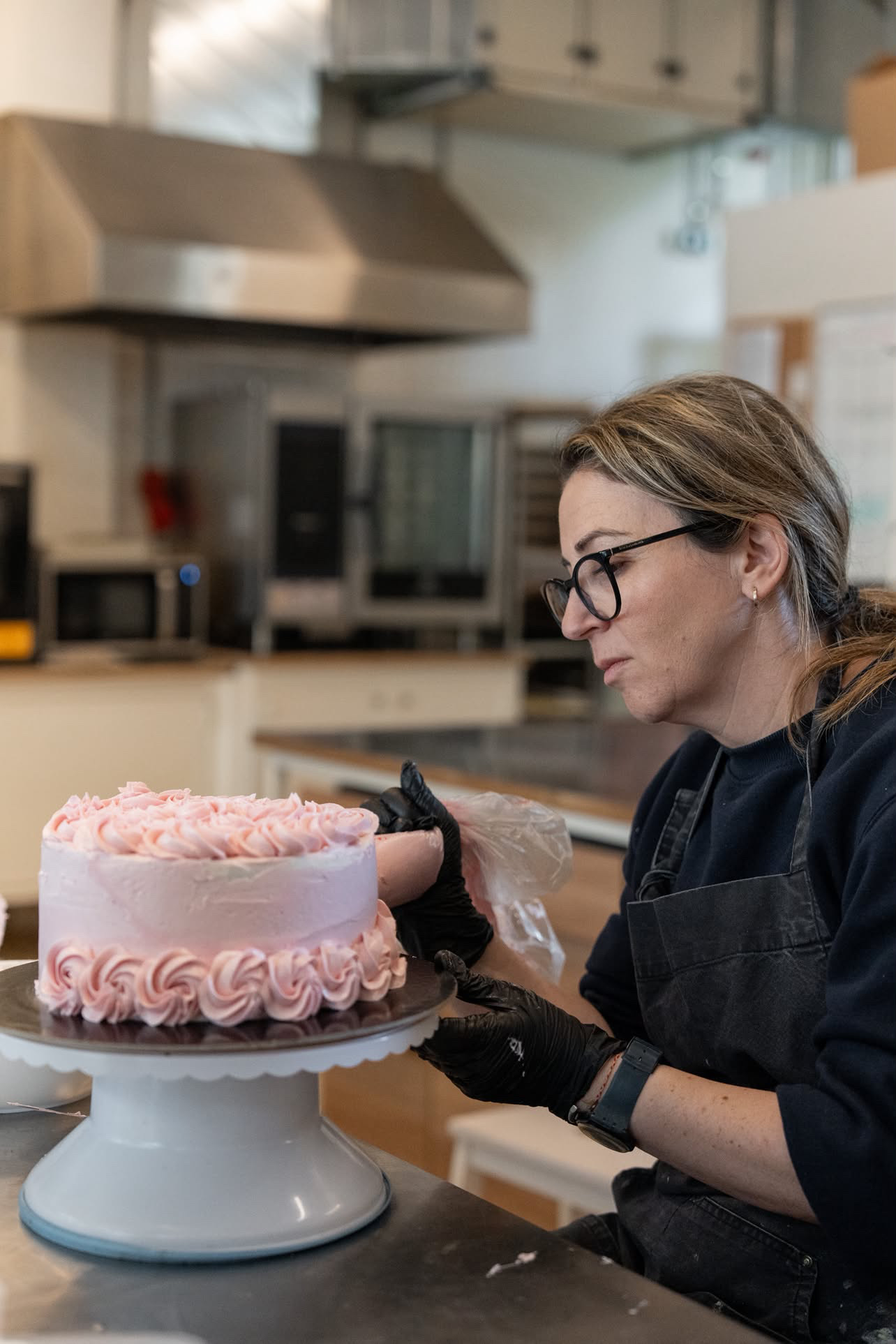 Kate piping a pink rose cake in the Black Eyed Kate kitchen